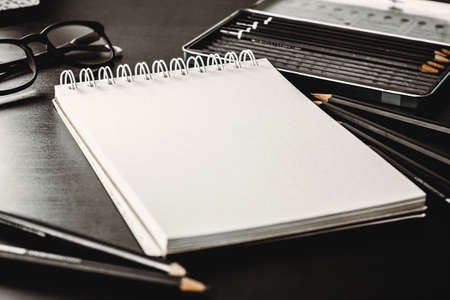 Blank notepad with white sheets on a dark table background. Writing diagonal mockup great for adding any drawing. Glasses and pencils in a background. Small focal length.の写真素材