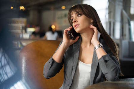 Young happy woman talking on mobile phone with friend while sitting alone in modern coffee shop interior, smiling hipster girl calling with cell telephone while relaxing after walking in summer dayの写真素材