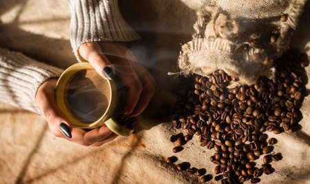 Female hands holding a cup of coffee with foam over wooden table, top view.の写真素材
