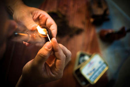 A man lighting a smoking pipe onder the wooden tableの写真素材