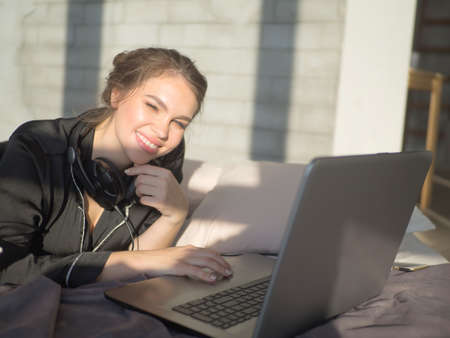 Portrait of Asian beautiful woman in pajama watch a laptop to surf internet, play social media, and work on bed and blanket in morning.の写真素材