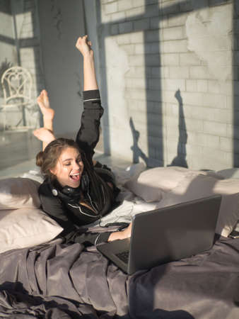 Happy brunette woman using laptop while sitting on bed in the morningの写真素材