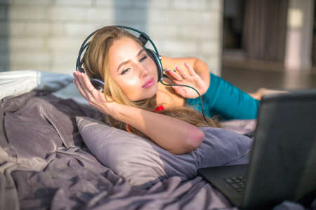 woman listening to music on a laptop while lying on the bed