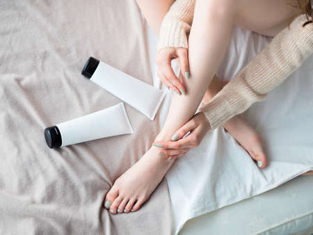 Beautiful young woman applying body lotion on bed sheet. Top view. Blank label for branding mock-up. Woman Skin Care Concept.の写真素材