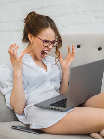 Student woman at table with laptop at home stressful, terrified in panic, shouting exasperated and frustrated. Unpleasant gesture. Annoying work drives me crazyの写真素材