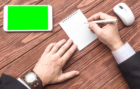 A top view of a hands of a businessman with a tablet PC and notebook on the wooden table. Man...