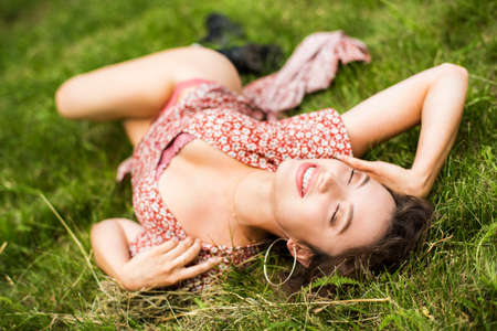 Girl in the grass. Beautiful young woman on the lawn. Lying in the grass, lying on the lawn in the park. Happy woman. A warm summer day. Inspiration.の写真素材