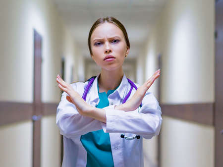 serious female doctor with stethoscope showing stop sign in hospital corridor. She cross her handsの写真素材