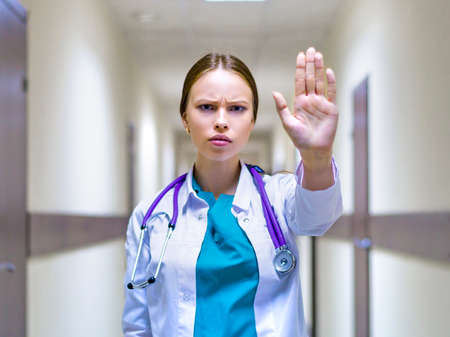 serious female doctor with stethoscope showing stop sign in the hospital corridorの写真素材