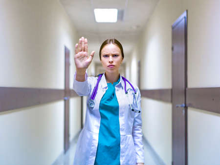 serious female doctor with stethoscope showing stop sign in the hospital corridorの写真素材