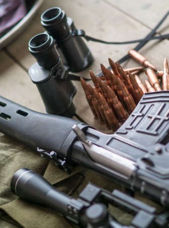 Sniper rifle, binoculars and ammunition on the wooden floor.