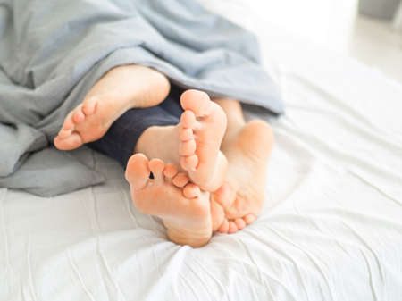 The legs from under the blanket. Young happy couple in bed at home