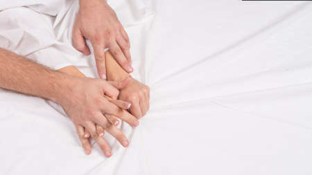 Sensual beautiful young couple is having sex on bed. Female hand pulling white sheets in ecstasy,...