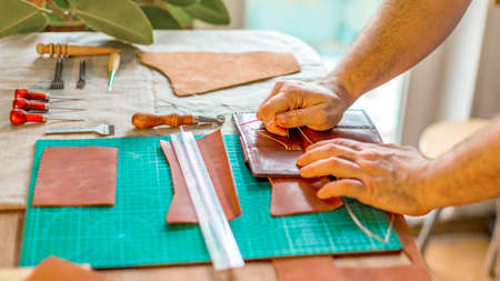 Close up hands of a leather craftsman working with leather textile at a workshop