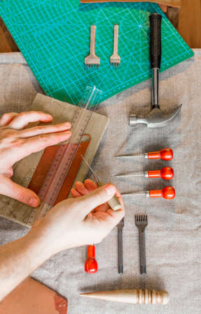 Close up hands of a leather craftsman working with leather textile at a workshop