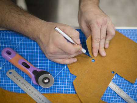 Man working with leather using crafting tools. Close up view of males hands cutting leather