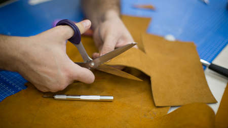 Man working with leather using crafting tools. Close up view of males hands cutting leather
