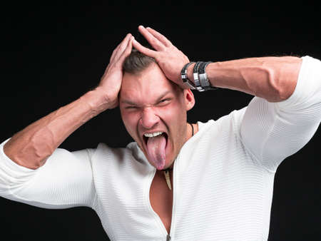 A funny man, wearing white sweater stuck out his tongue over dark backgroundの写真素材