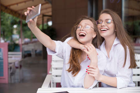 two happy girls making a selfie in summer cafeの写真素材