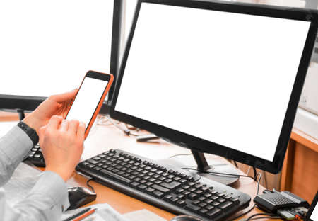 Woman in the office in front of monitors. Closeup of a hand with a phone.