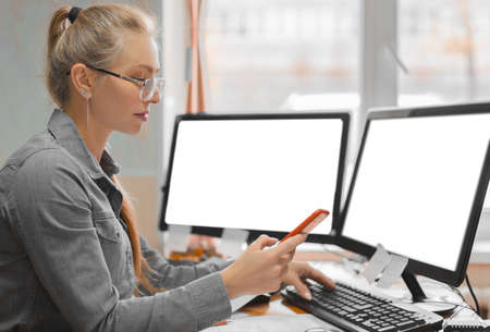 Woman holding smartphone and using computer in office room, for graphics display montage