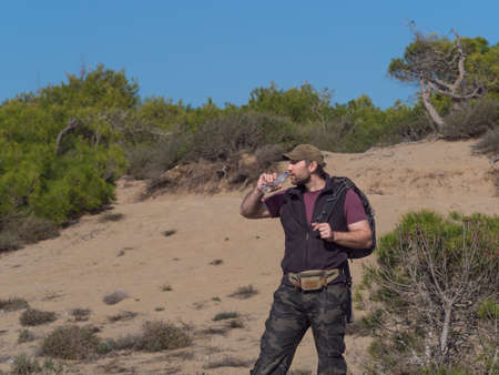 Tourist man drinking water from the plastic bottle in a desert walk.