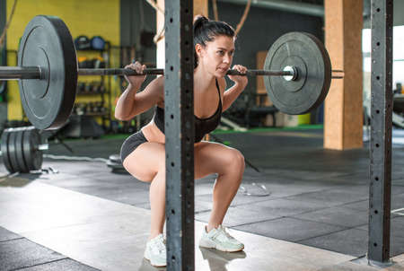 Photo of a woman is lifting weight while working out with barbell in gym.の写真素材