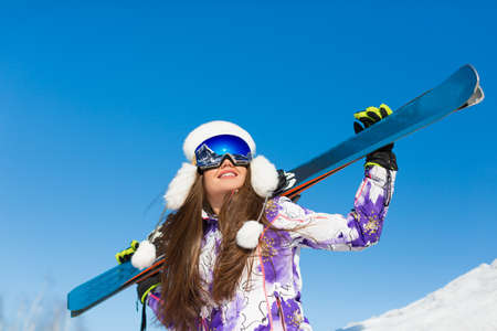 Winter portrait of a young sporty woman with a ski on a mountain peak over sky background.の写真素材
