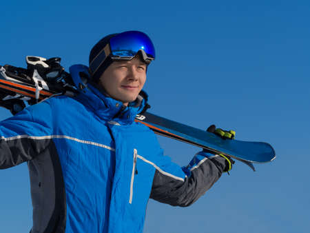Close up portrait of a man with a ski on a mountain peak over blue sky background. Active lifestyle conceptの写真素材