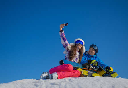 Cheerful young loving couple making winter selfie on a mountain peak during a vacation on a ski resort.の写真素材