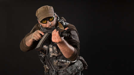 A mercenary with a gun aims at the enemy. Close-up on a dark background.の写真素材