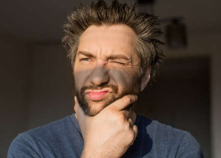 Funny man after waking scratches his beard, looking at the morning sun.