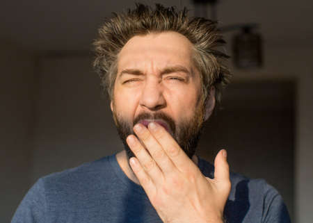Man with a beard after waking up yawns, looking at the morning sun.の写真素材
