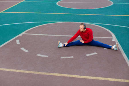 A young man stretches muscles after a hard workout on the sports ground early in the morning.
