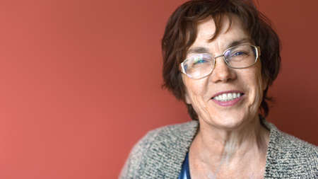 Close up portrait of a happy smiling elder woman over dark red background.