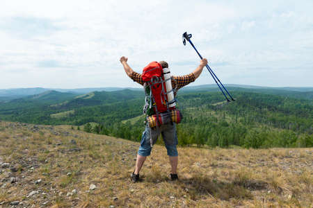 Middle aged hiker backpacker man growing hands with trekking poles during high altitude...