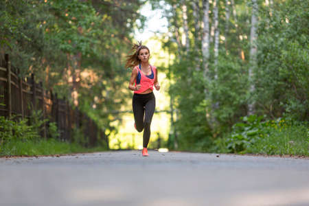 Sportswoman runs along the road in the forest.