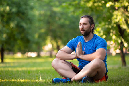 Bearded man in lotus pose outdoor.