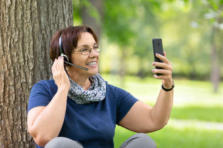 A senior woman enjoying a beautiful spring day in the citys central park. She having a video call.