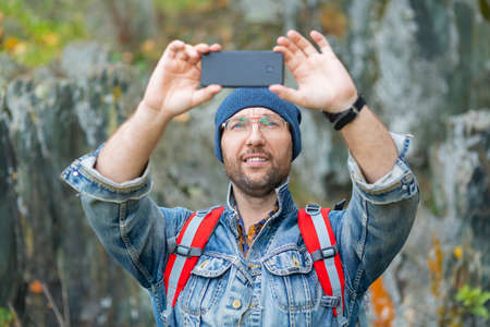 Smiling middle aged hiker taking a photo with his mobile phone.の写真素材