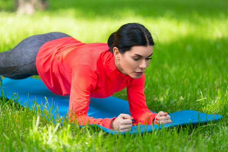 Woman doing plank exercise on a grass in city park. Closeup.