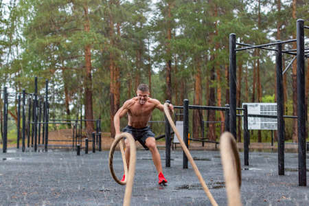Photo of a man having hard workout with a ropes outdoor in a rainy day.