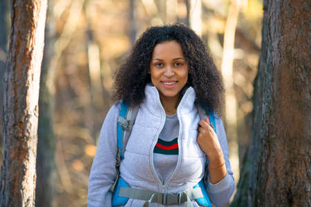 Smiling african american woman with backpack in a forest.