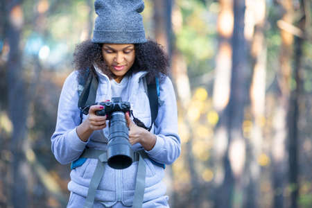 African American woman in the forest with a camera. Shee looks at cameras monitor.の写真素材