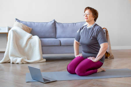 Senior woman meditating in front of laphop monitor.の写真素材