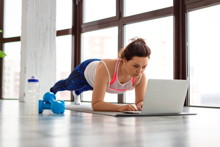 Middle-aged woman exercising at home online in front of a laptop monitor. In plank position.の写真素材