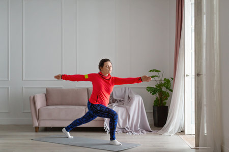 Middle aged woman practices yoga at home. Archer Pose.の写真素材