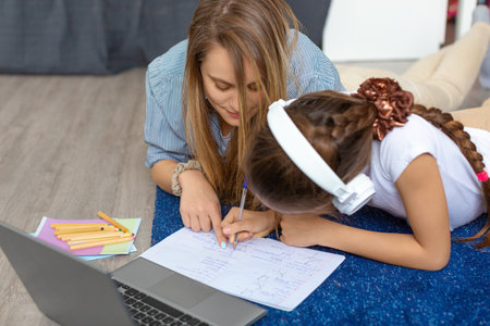 Mom helps her daughter to do homework in front of a laptop monitor while lying on the floor.の写真素材