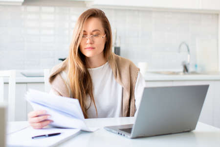 Photo of a woman in front of laptop monitor working with papers.の写真素材
