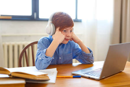 Close-up photo sad boy pupil in headphones in front of a laptop monitor during an online lesson